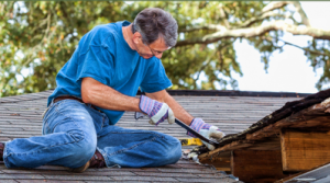 A worker is sitting and repairing the top roof of a house.