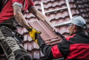 Two technicians hand each other roofing materials to complete an installation.